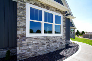 Side of suburban home with wraparound sidewalk, brick exterior, and three large white-frame windows.